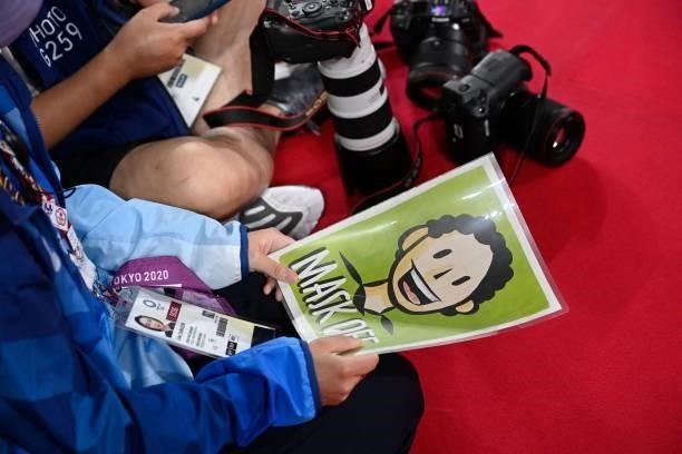 Photo manager holds a sign to indicate to athletes when they are permitted to take off their face masks at the medal ceremony for the men's doubles...
