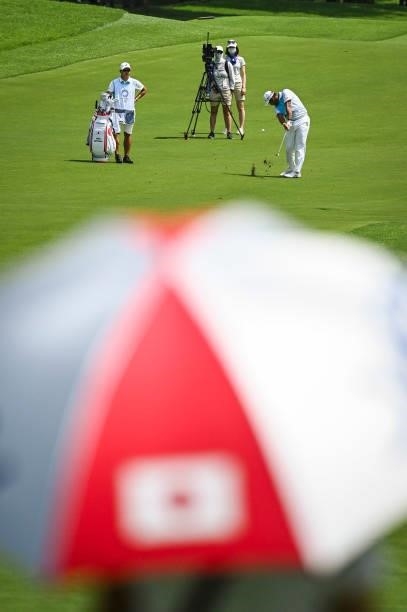 Hideki Matsuyama of Team Japan plays his approach shot on the ninth hole fairway as a fan with a Japan umbrella watches during the final round of...