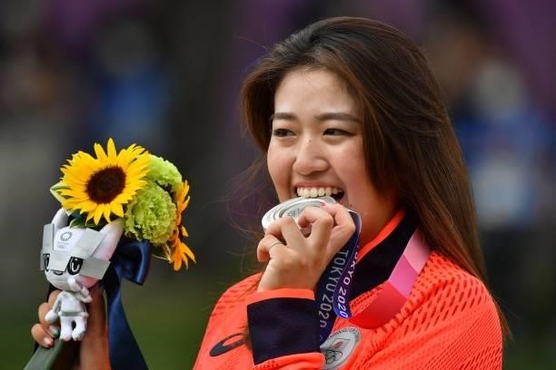 Silver medallist Japan's Mone Inami bites her medal on the podium during the victory ceremony of the womens golf individual stroke play during the...
