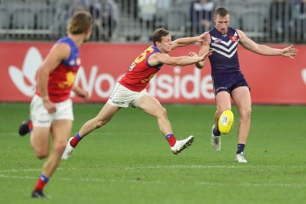 Josh Treacy of the Dockers kicks the ball under pressure from Ryan Lester of the Lions during the 2021 AFL Round 21 match between the Fremantle...