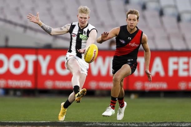 John Noble of the Magpies kicks the ball ahead of Darcy Parish of the Bombers during the 2021 AFL Round 23 match between the Essendon Bombers and the...