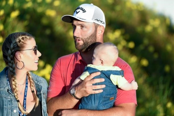Jon Rahm of Spain holds his baby while standing with his wife, Kelley Cahill, and watching the playoff during the weather delayed final round of THE...
