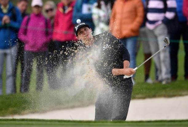 John Catlin of United States plays a bunker shot at the 15th hole with an awkward stance during Day Three of The Omega European Masters at...