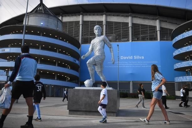 Supporters walk past the newly-unveiled statue of former Manchester City footballer David Silva outside the stadium ahead of the English Premier...