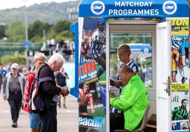 Fans buy Matchday programmes from a man and a boy in a kiosk ahead of the Premier League match between Brighton & Hove Albion and Everton at American...