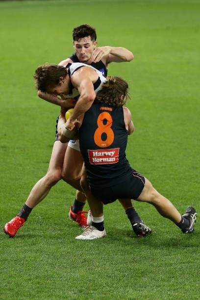 Tom Atkins of the Cats is tackled by Lachie Ash and Callan Ward of the Giants during the 2021 AFL Second Semi Final match between the Geelong Cats...