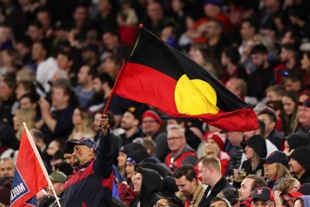 The Melbourne cheer squad hold aloft the aboriginal flag during the 2021 AFL First Preliminary Final match between the Melbourne Demons and the...