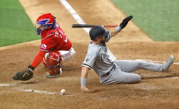 Romy Gonzalez of the Chicago White Sox slides across the plate to score as Jose Trevino of the Texas Rangers has the ball get past him during the...