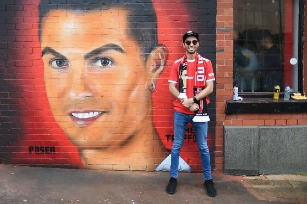 Manchester United fan poses next to a mural of Cristiano Ronaldo of Manchester United painted on a wall before the Premier League match between...