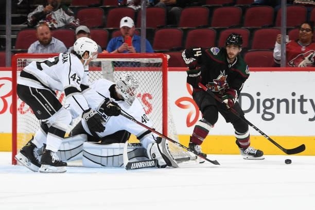 Shayne Gostisbehere of the Arizona Coyotes skates the puck around the back of the net while being defended by Cal Peterson and Martin Chromiak of the...