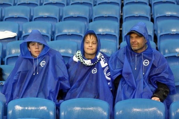 Three Brighton fans in rain ponchos sit on wet seats during the Premier League match between Brighton & Hove Albion and Arsenal at American Express...