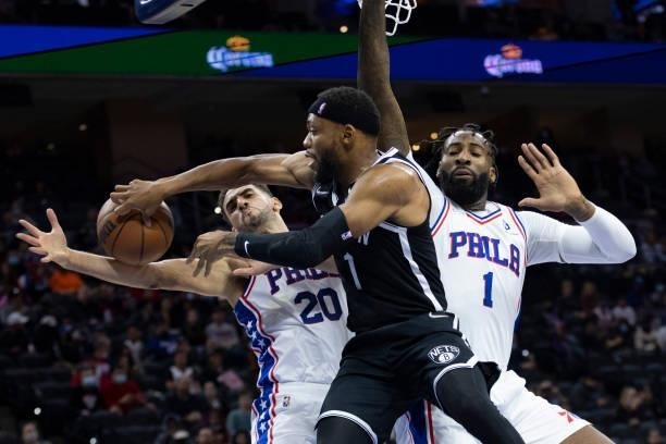 Bruce Brown of the Brooklyn Nets passes the ball against Georges Niang and Andre Drummond of the Philadelphia 76ers in the second half at the Wells...