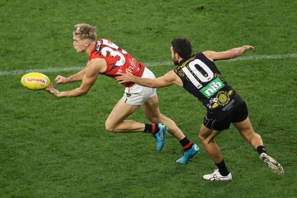 Matt Guelfi of the Bombers handballs against Shane Edwards of the Tigers during the round 12 AFL match between the Essendon Bombers and the Richmond...