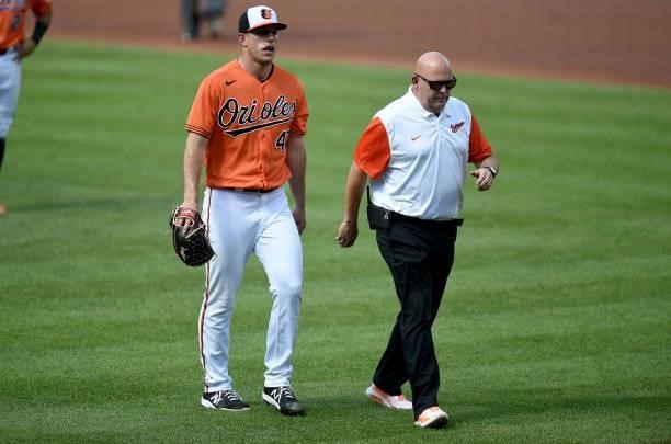 John Means of the Baltimore Orioles walks off the field with head trainer Brian Ebel in the first inning against the Cleveland Indians at Oriole Park...