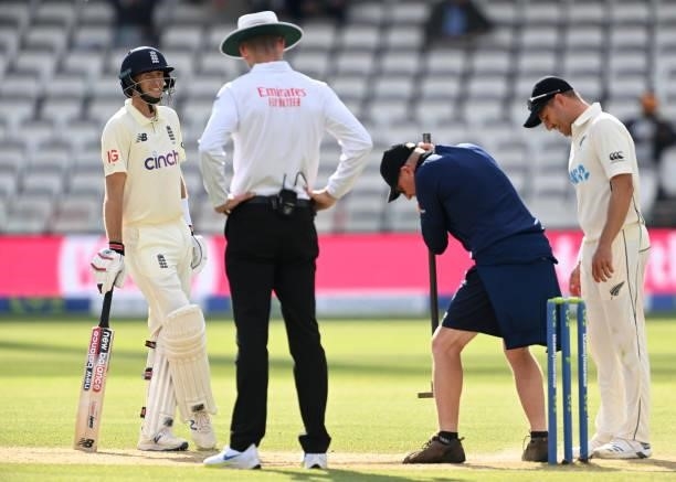 Joe Root of England talks to umpire Michael Gough as a member of staff prepares foot holes for Neil Wagner of New Zealand during Day 5 of the First...