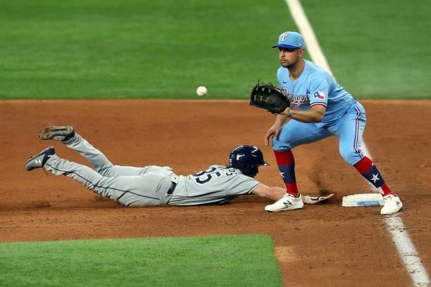 Brett Phillips of the Tampa Bay Rays dives back ahead of the pickoff throw to Nate Lowe of the Texas Rangers in the fifth inning at Globe Life Field...