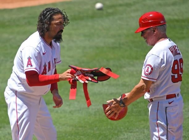 Anthony Rendon hands over his protective batting gear to first base coach Bruce Hines of the Los Angeles Angels in the game against the Los Angeles...