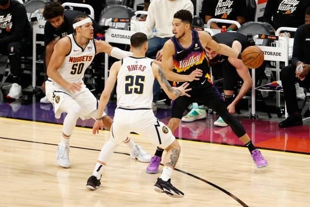 Devin Booker of the Phoenix Suns handles the ball against Aaron Gordon and Austin Rivers of the Denver Nuggets during the first half in Game One of...
