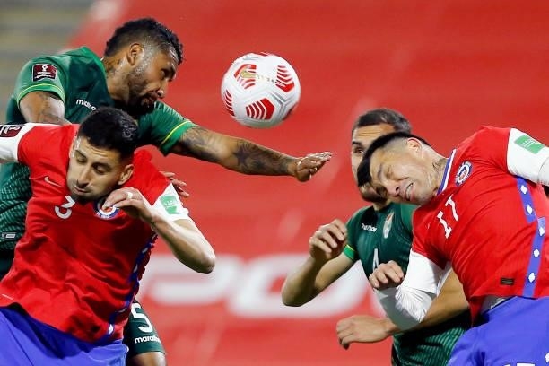 Adrián Jusino of Bolivia jumps for the ball with Guillermo Maripán and Gary Medel of Chile during a match between Chile and Bolivia as part of South...
