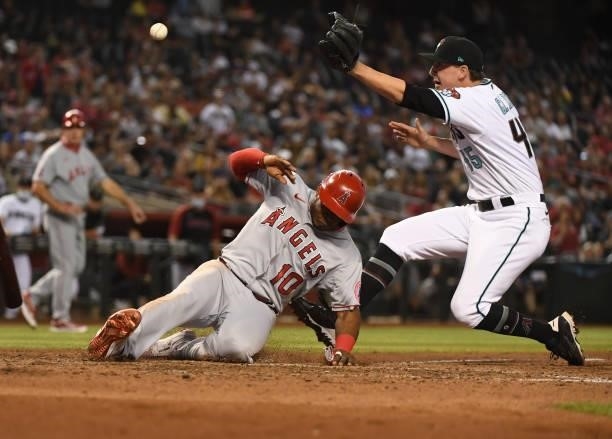 Justin Upton of the Los Angeles Angels slides safely into home plate as the throw from Carson Kelly of the Arizona Diamondback gets away from Taylor...
