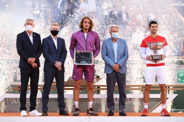 Runner-up Stefanos Tsitsipas of Greece and winner Novak Djokovic of Serbia pose with their respective trophies on the podium with the presentation...