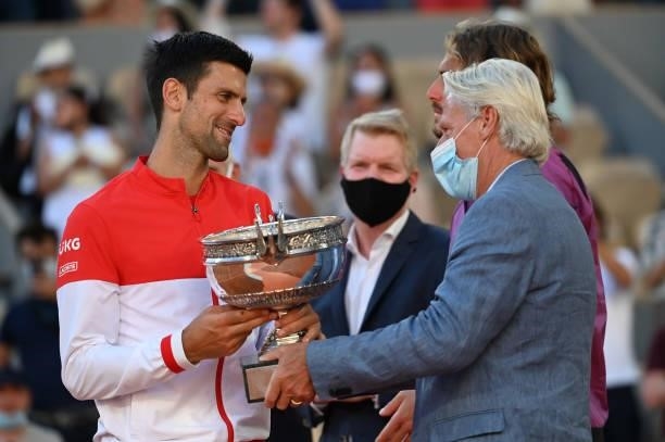 Winner Novak Djokovic of Serbia receives the trophy from Bjorn Borg while Jim Courier look on during the trophy ceremony for the Men's Singles final...