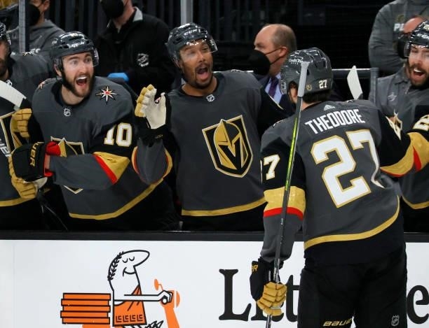 Shea Theodore of the Vegas Golden Knights celebrates with teammates Nicolas Roy and Keegan Kolesar on the bench after Theodore assisted Alec Martinez...