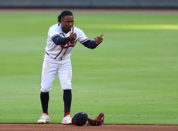 Ozzie Albies of the Atlanta Braves puts his hat and glove on the ground as he motions towards Alex Verdugo of the Boston Red Sox at first base during...