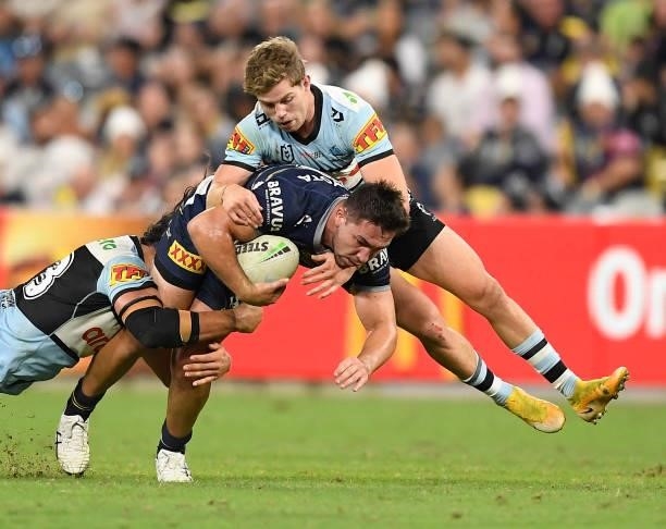 Reece Robson of the Cowboys is tackled by Blayke Brailey and Toby Rudolf of the Sharks during the round 15 NRL match between the North Queensland...