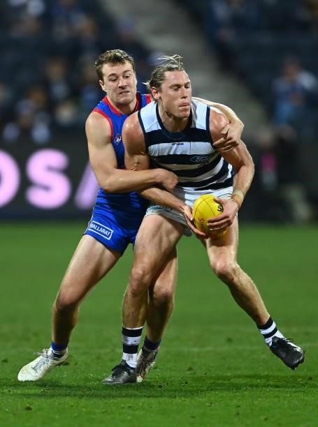 Mark Blicavs of the Cats handballs whilst being tackled by Jackson Macrae of the Bulldogs during the round 13 AFL match between the Geelong Cats and...