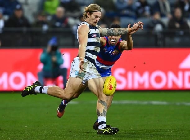 Tom Stewart of the Cats kicks whilst being tackled by Jason Johannisen of the Bulldogs during the round 13 AFL match between the Geelong Cats and the...
