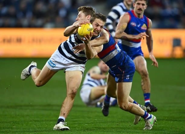 Tom Atkins of the Cats is tackled by Lachie Hunter of the Bulldogs during the round 13 AFL match between the Geelong Cats and the Western Bulldogs at...