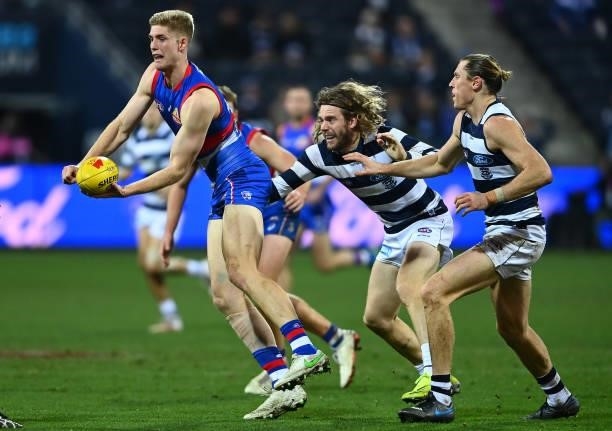 Tim English of the Bulldogs handballs whilst being tackled by Cameron Guthrie of the Cats during the round 13 AFL match between the Geelong Cats and...