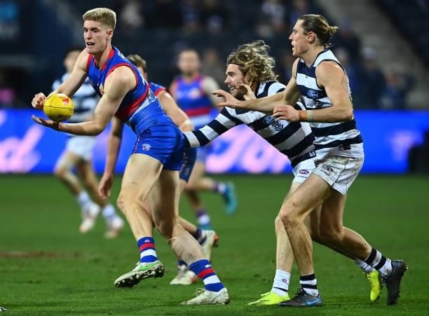 Tim English of the Bulldogs handballs whilst being tackled by Cameron Guthrie of the Cats during the round 13 AFL match between the Geelong Cats and...
