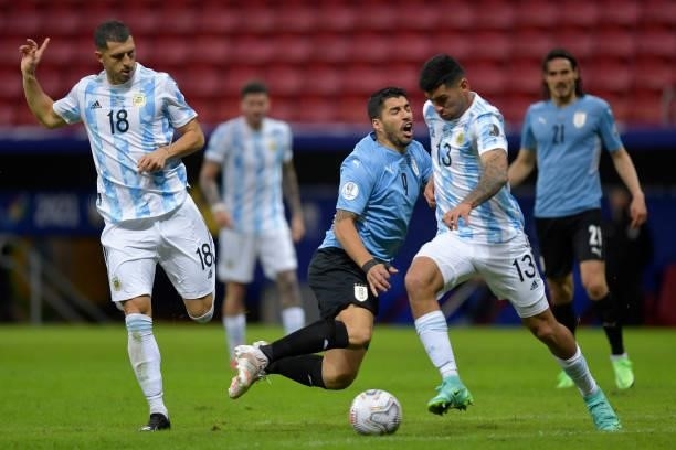 Luis Suarez of Uruguay falls down against Cristian Romero and Guido Rodriguez of Argentina during a group A match between Argentina and Chile as part...