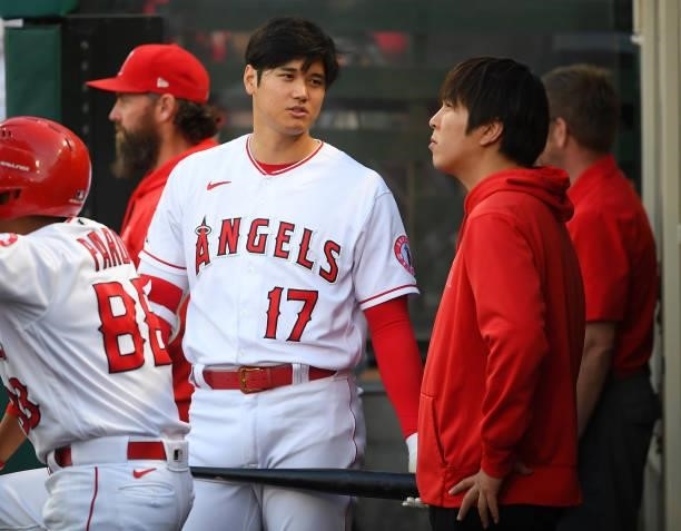 Shohei Ohtani of the Los Angeles Angels talks with his translator Ippei Mizuhara in the dugout during the game against the Detroit Tigers at Angel...