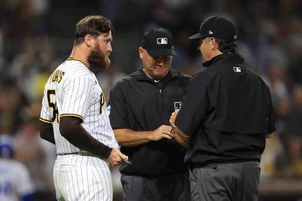 Austin Adams of the San Diego Padres has his glove inspected for foreign substances by umpire Mark Carlson and umpire James Hoye during the seventh...