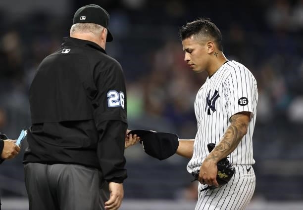 Third base umpire Bill Miller checks the hat and glove of Jonathan Loaisiga of the New York Yankees as he is pulled from the game in the eighth...