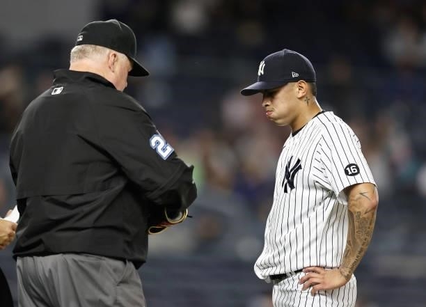 Third base umpire Bill Miller checks the hat and glove of Jonathan Loaisiga of the New York Yankees as he is pulled from the game in the eighth...