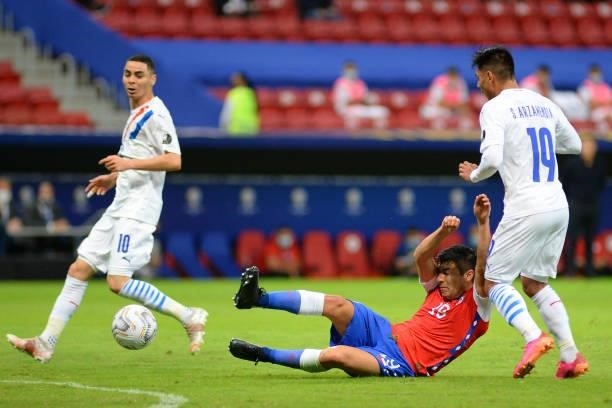 Tomás Alarcón of Chile falls down as he fights for the ball against Miguel Almiron and Santiago Arzamendia of Paraguay during a Group A match between...