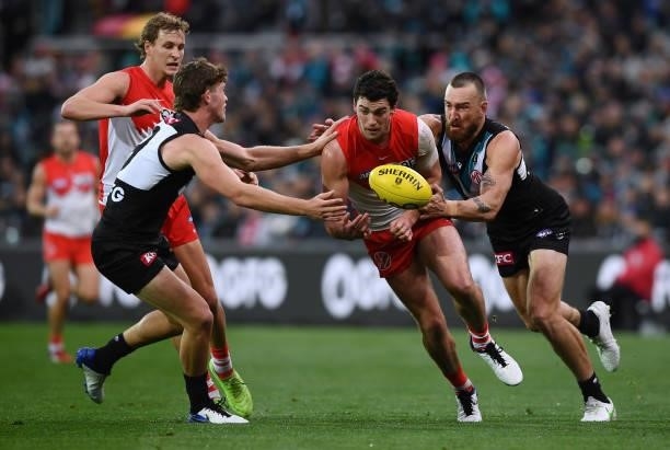 Tom McCartin of the Swans handballs between Mitch Georgiades of Port Adelaide and Charlie Dixon of Port Adelaide during the round 15 AFL match...