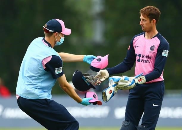 John Simpson of Middlesex swapping his helmet for a cap with a staff member during the Vitality Blast T20 match between Middlesex and Glamorgan at...