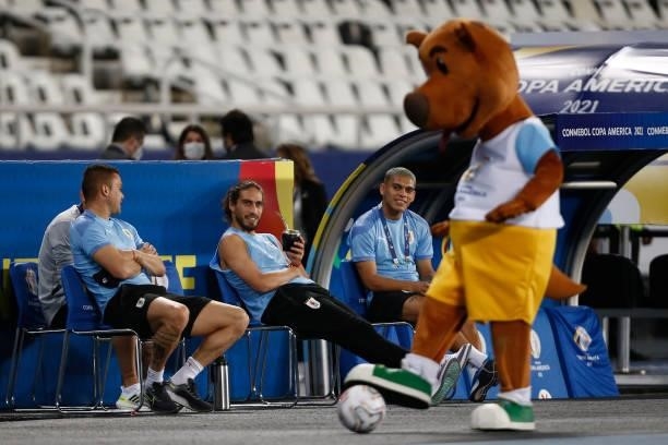 Martín Caceres of Uruguay drinks mate next to teammate Brian Ocampo as watching official tournament mascot Pibe before a group A match between...