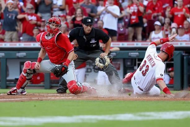 Jesse Winker of the Cincinnati Reds slides into home plate for a run past Andrew Knapp in the third inning at Great American Ball Park on June 28,...
