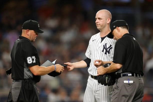 Lucas Luetge of the New York Yankees hands his hat and glove to umpires Scott Barry and Dan Iassogna to check during the sixth inning against the Los...