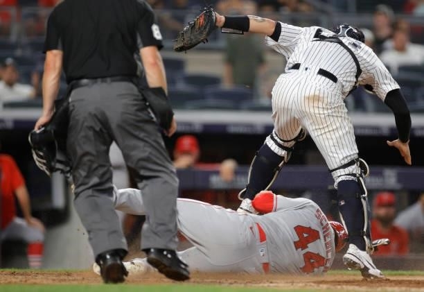 Scott Schebler of the Los Angeles Angels slides safely into home to score as Gary Sanchez of the New York Yankees leaps above him to make a catch...