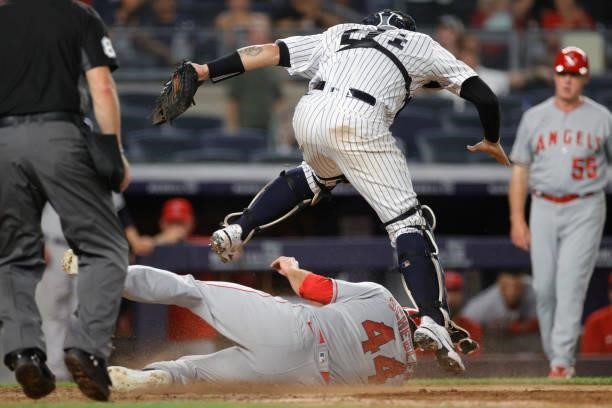 Scott Schebler of the Los Angeles Angels slides safely into home to score as Gary Sanchez of the New York Yankees leaps above him to make a catch...
