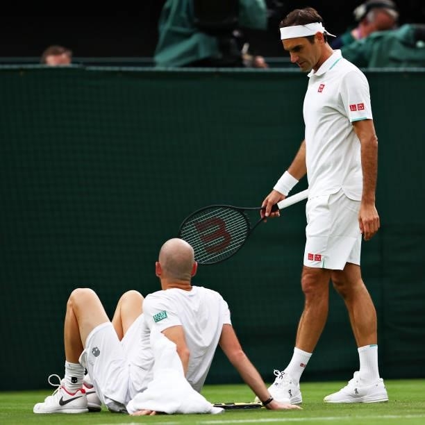 Roger Federer of Switzerland checks on his opponent Adrian Mannarino of France who reacts after going down with an injury during their Men's Singles...
