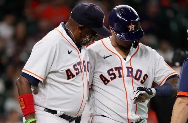 Martin Maldonado of the Houston Astros walks to first alongside manager Dusty Baker Jr. #12 after being hit on the hand by a pitch from Travis Lakins...