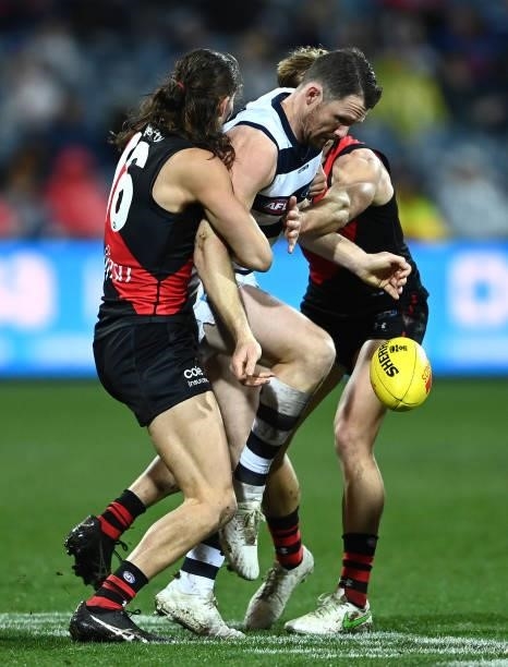 Patrick Dangerfield of the Cats kicks whilst being tackled by Archie Perkins of the Bombers during the round 16 AFL match between Geelong Cats and...